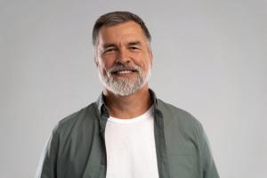 Smiling man with grey hair and beard wearing a green shirt.
