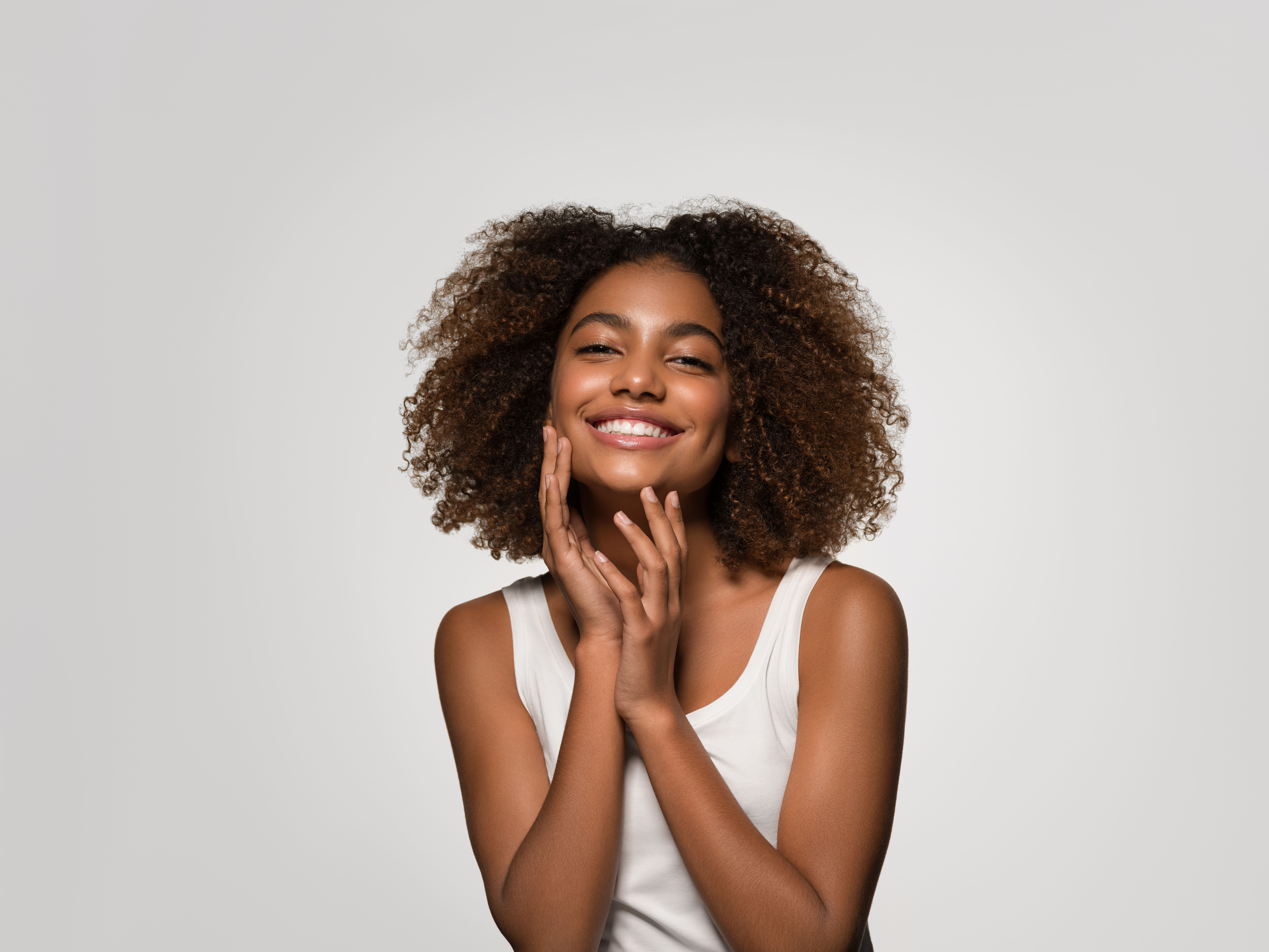 a woman with curly hair is smiling and touching her face .