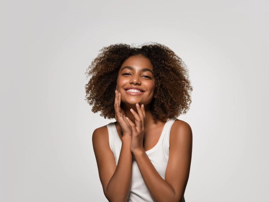 a woman with curly hair is smiling and touching her face .