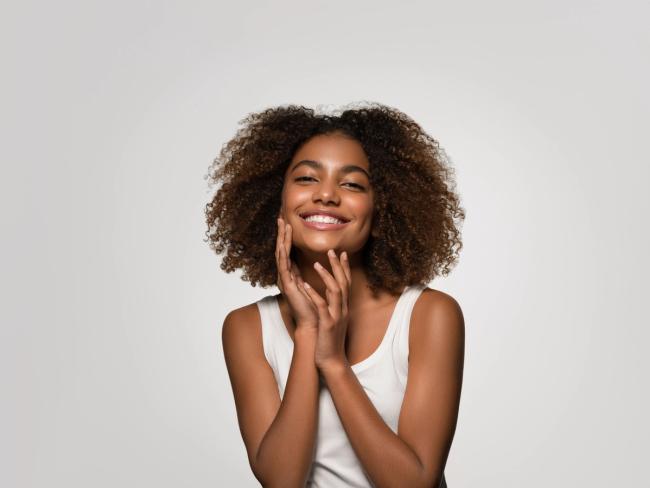Smiling Black woman with curly hair touching her face.