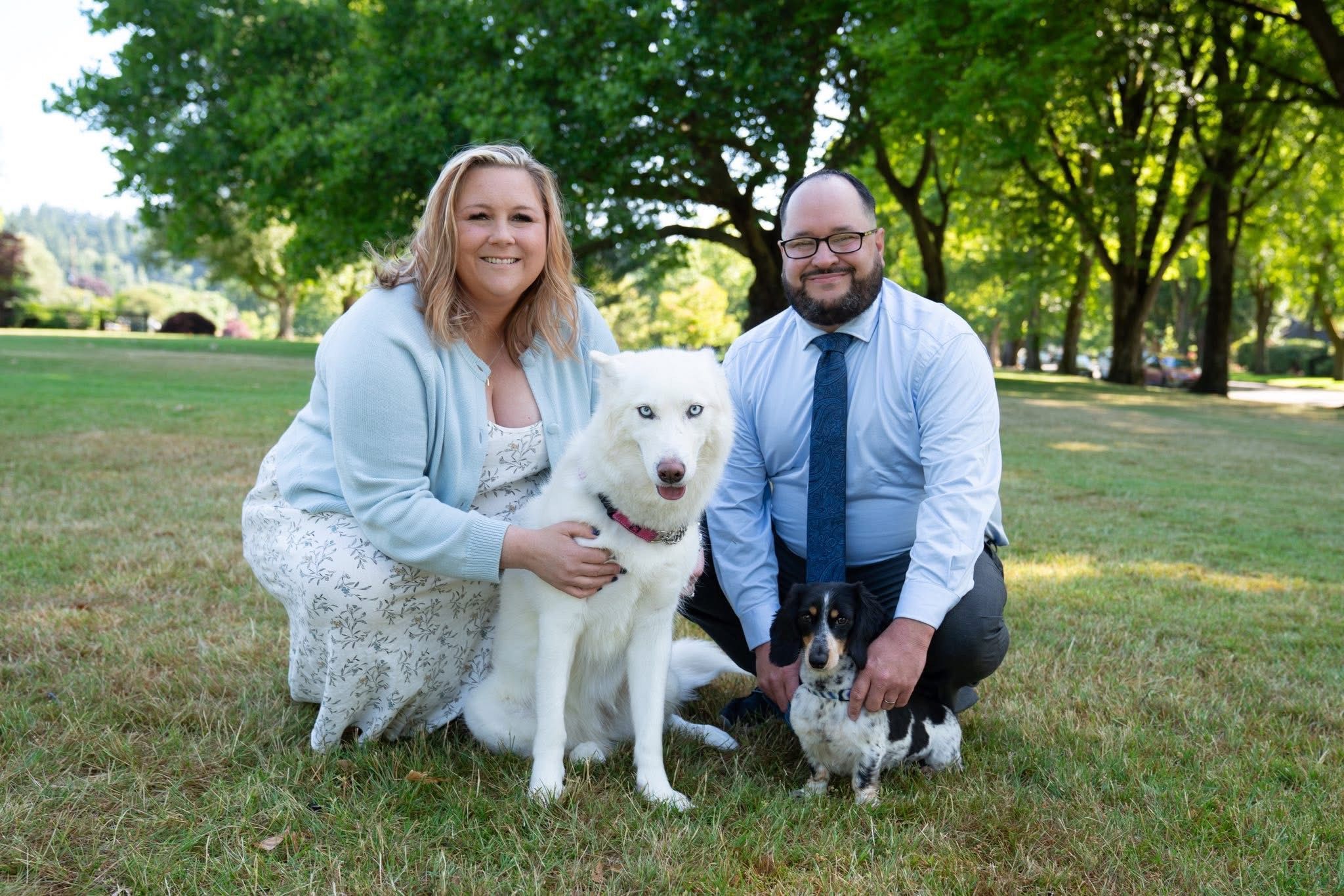 a man and woman are posing for a picture with their dog in a park .