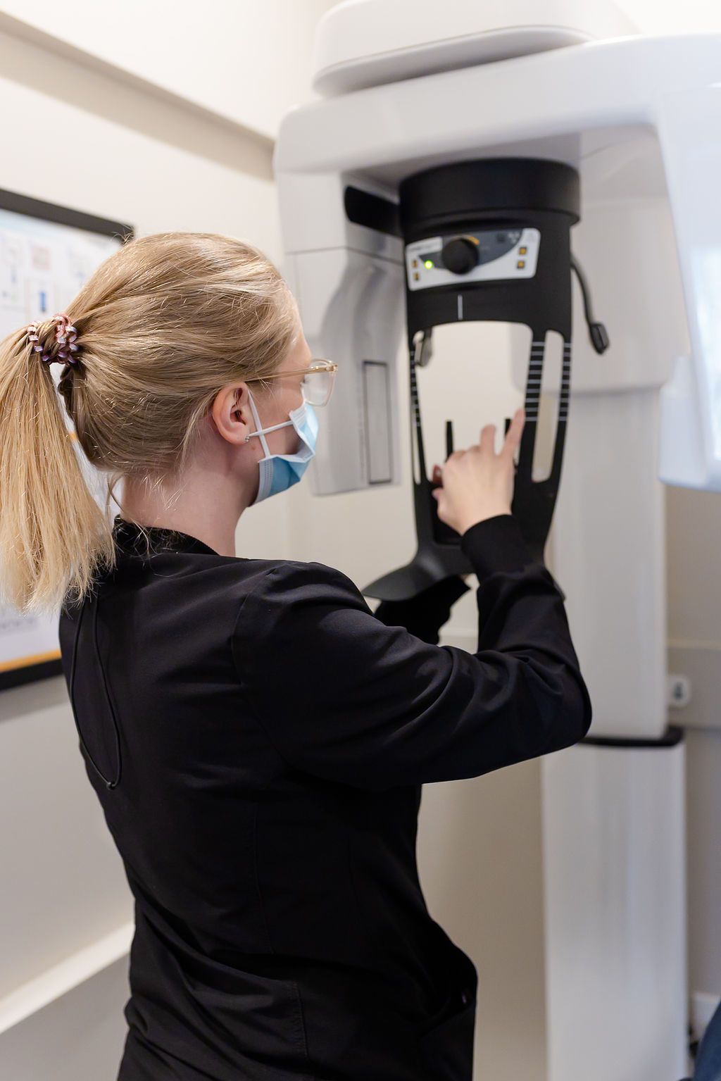 A masked dental professional adjusts a dental panoramic X-ray machine.