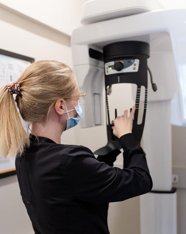 A masked dental professional adjusts a dental panoramic X-ray machine.