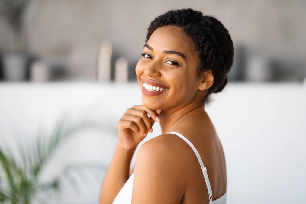 A smiling Black woman with braided hair looks over her shoulder.