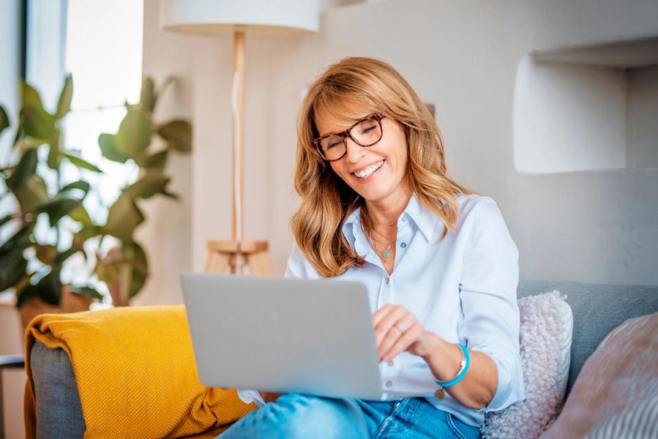 a woman is sitting on a couch using a laptop computer .