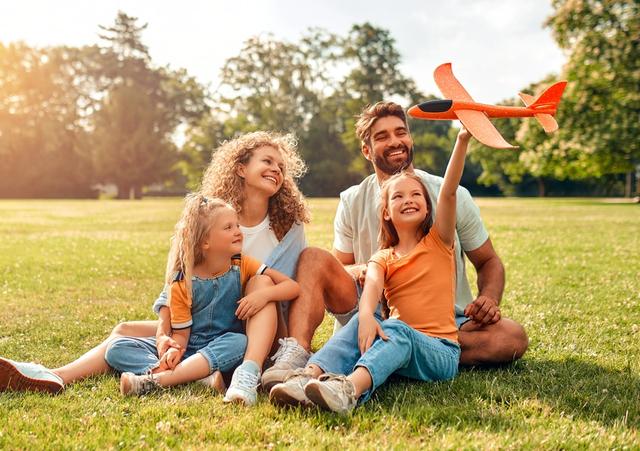 a family is sitting on the grass in a park with a toy airplane .
