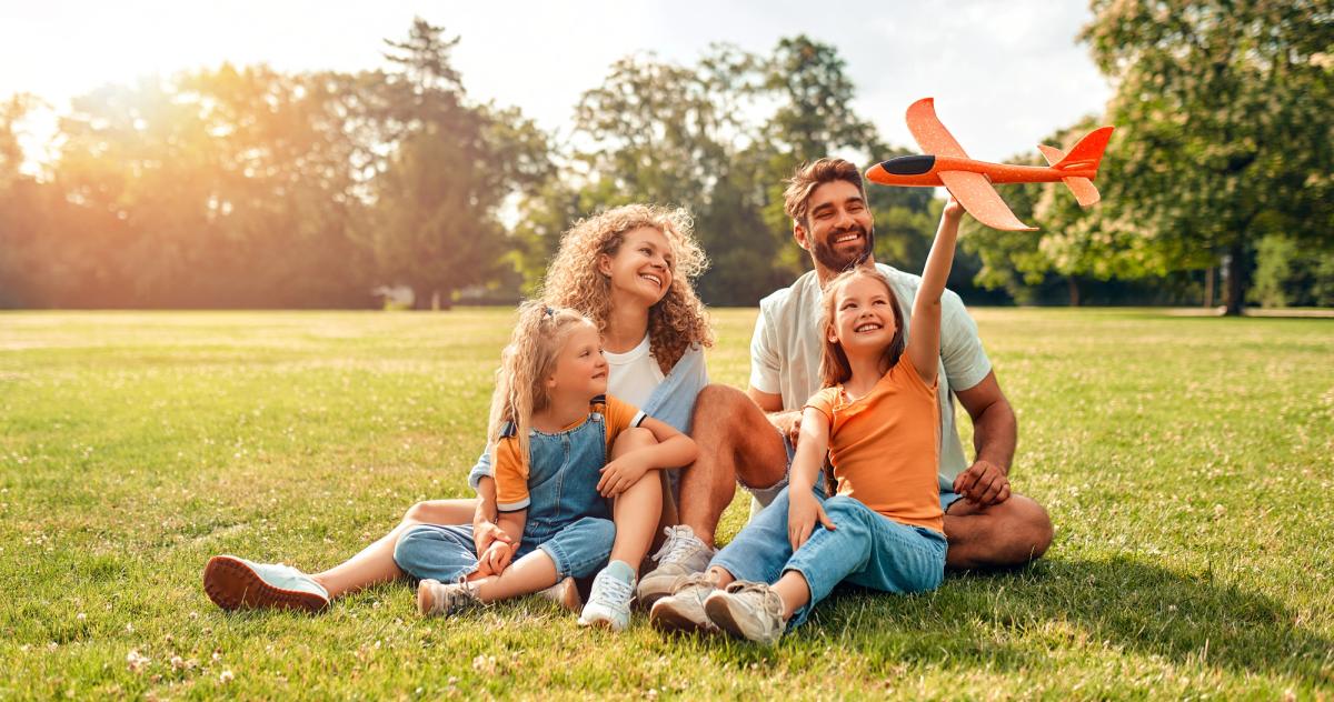 a family is sitting on the grass in a park with a toy airplane .