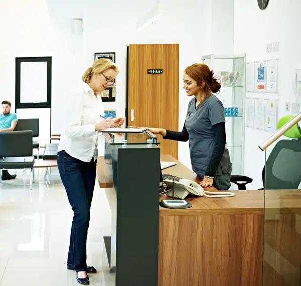 a woman is standing at a counter in a dental office talking to a nurse .