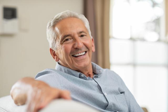 an elderly man is sitting on a couch and smiling .