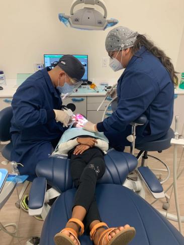 a little girl is laying in a dental chair while two dentists work on her teeth