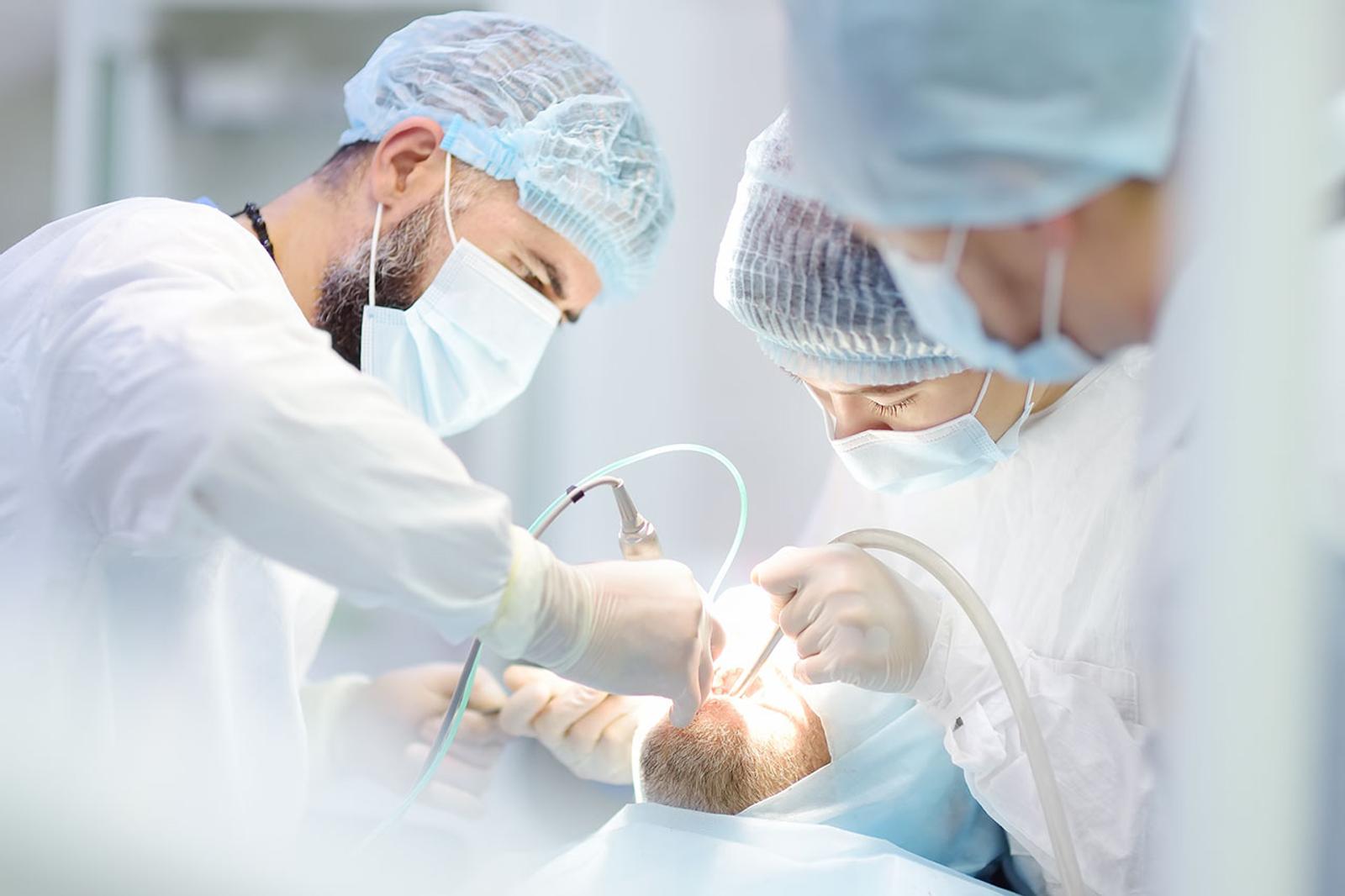 a group of dentists are working on a patient 's teeth in an operating room.