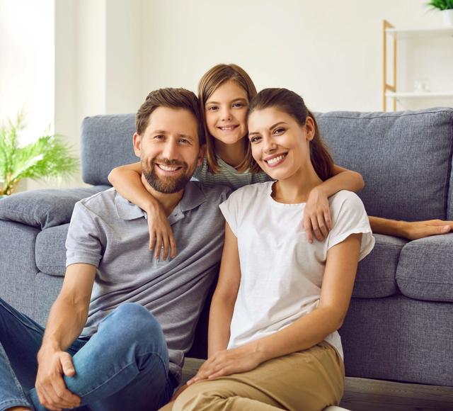a family is posing for a picture while sitting on the floor in front of a couch .