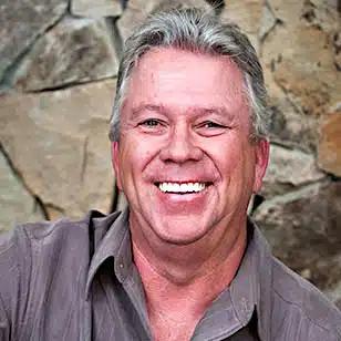 a man is smiling in front of a stone wall .
