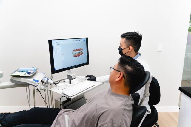 A dentist and patient view a 3D dental model on a computer screen.