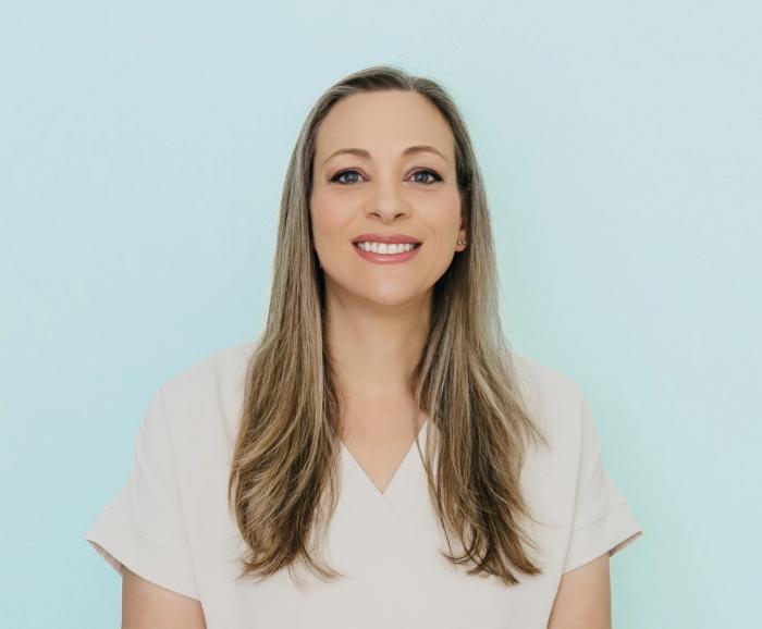Smiling woman with long blonde and gray hair against a light blue background.