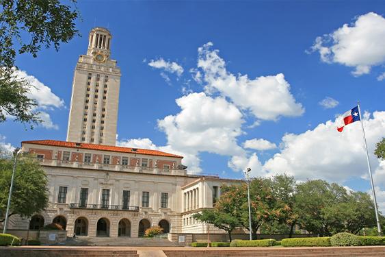 a large building with a clock tower and a texas flag flying in front of it .
