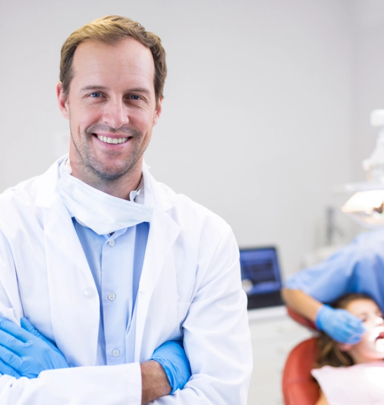 a smiling dentist with his arms crossed in front of a patient