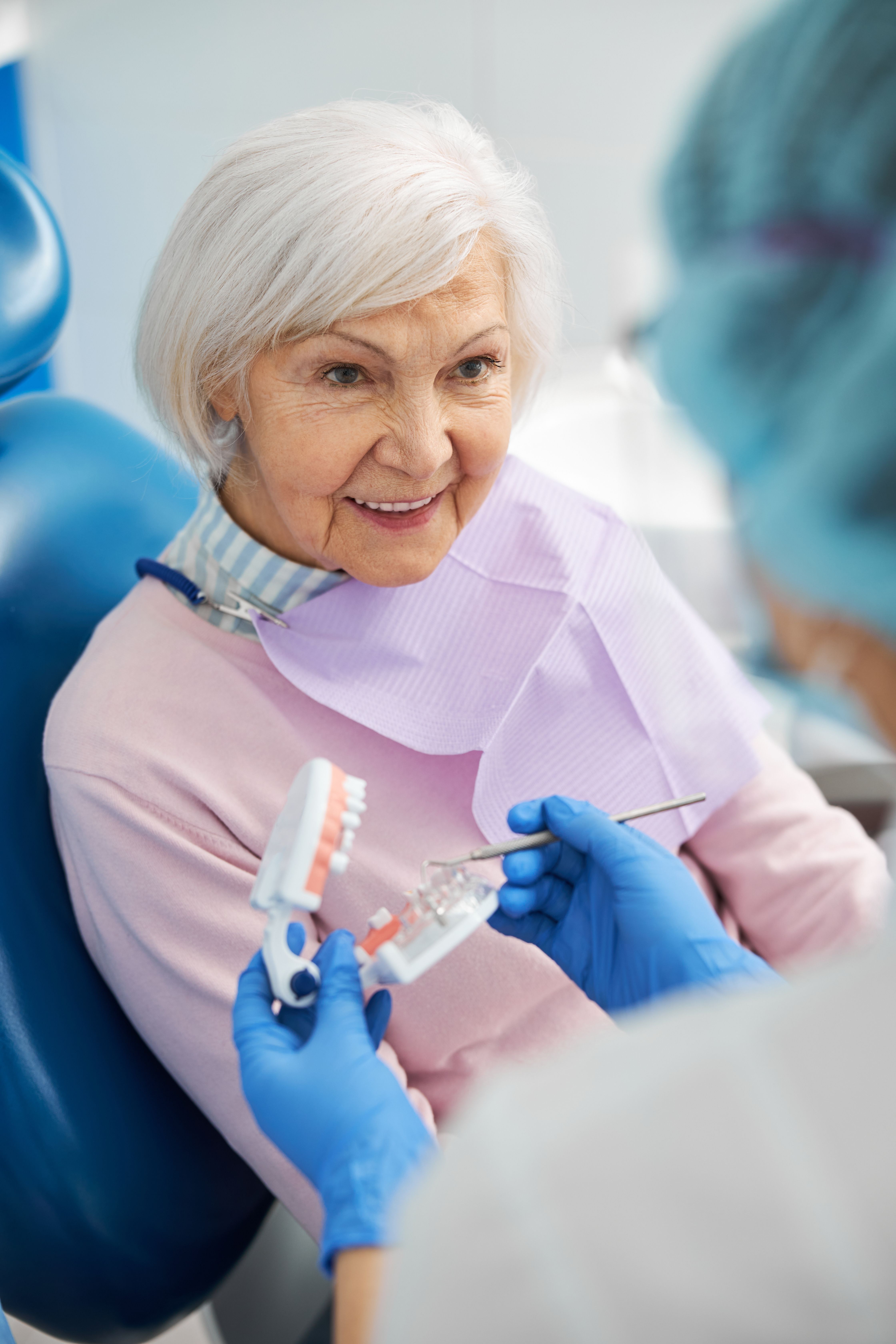 an elderly woman is sitting in a dental chair while a dentist holds a model of her teeth .