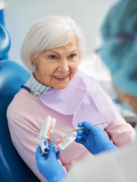 an elderly woman is sitting in a dental chair while a dentist holds a model of her teeth .