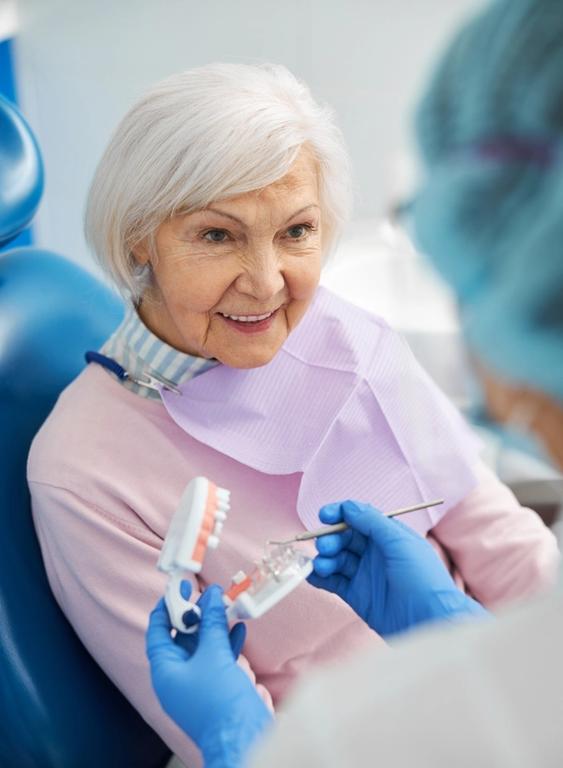an elderly woman is sitting in a dental chair while a dentist holds a model of her teeth .