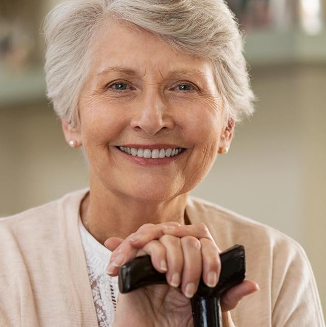 an elderly woman is smiling while holding a cane .