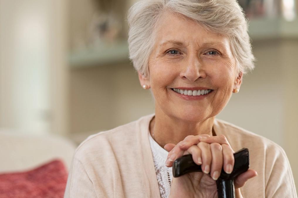 Smiling older woman with grey hair holding a cane.