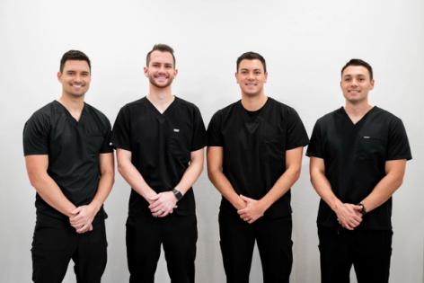 a group of four men in black scrubs are standing next to each other .