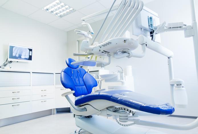an empty dental office with a blue dental chair and dental equipment .