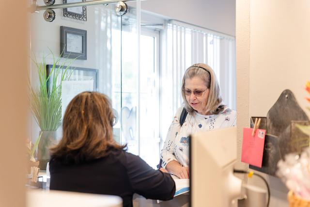 a woman is sitting at a counter in a dental office talking to another woman .