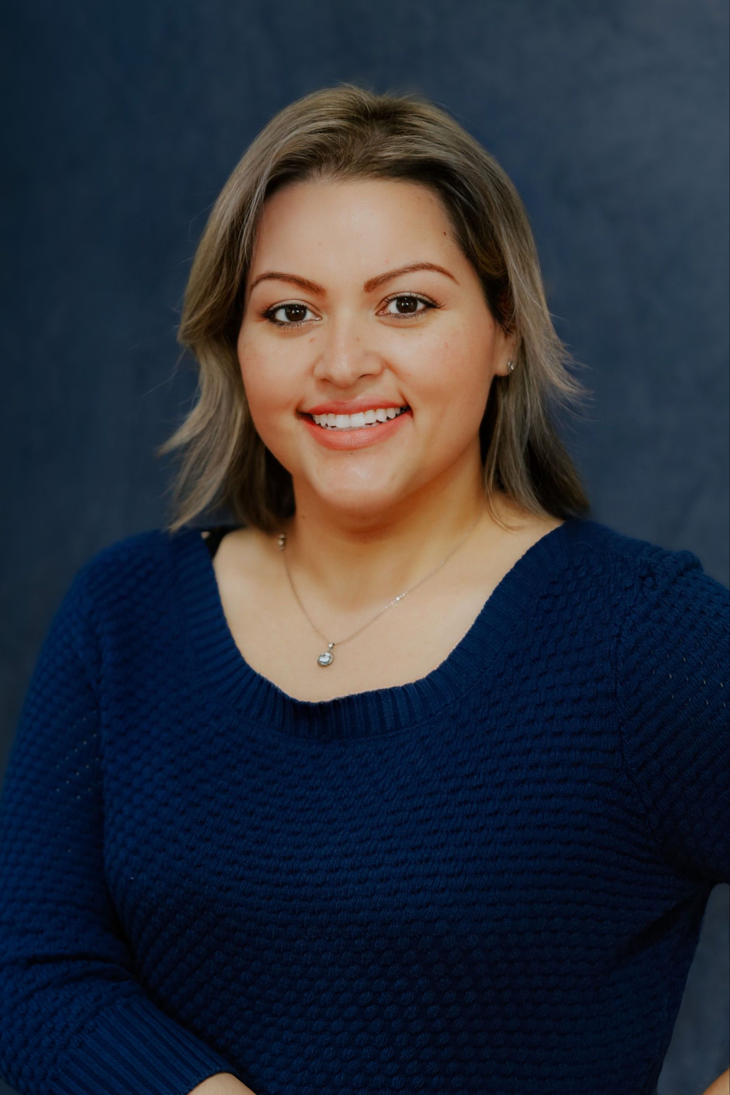 a woman wearing a blue sweater and a necklace smiles for the camera