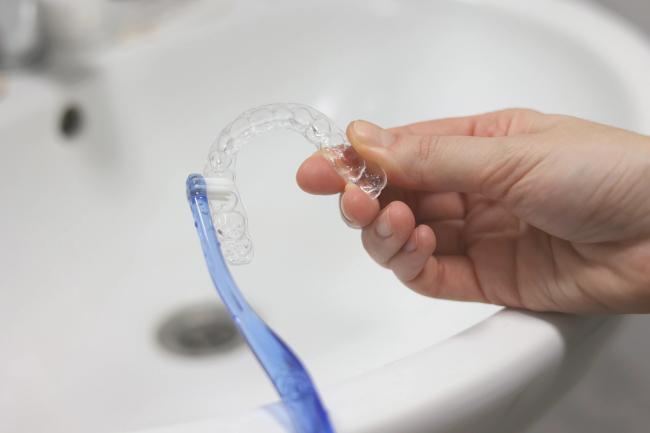 a person is holding an invisalign tray next to a toothbrush in a bathroom sink .