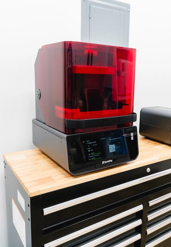 SprintRay Pro 2 3D printer with a red transparent cover and display screen on a wooden countertop.