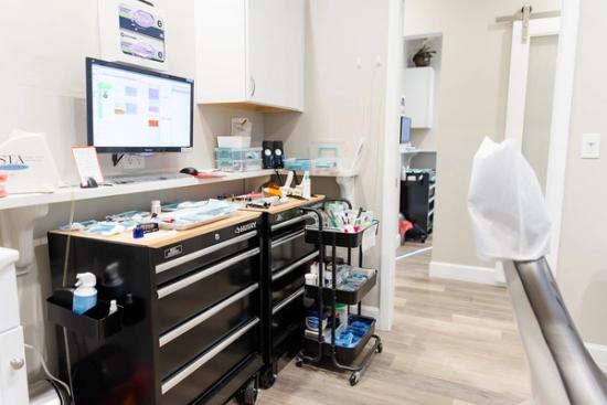 a dental office with a desk , chair , computer , and tools .