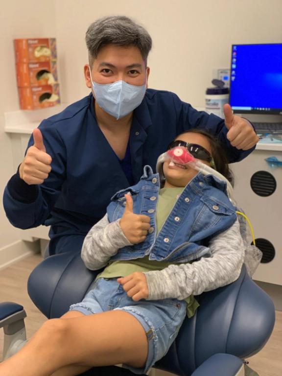 a little girl in a dental chair giving a thumbs up