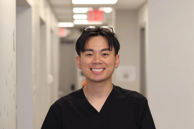 a young man in a black scrub is smiling in a hallway .