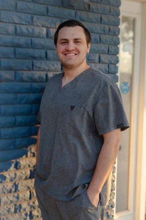 a man wearing a grey scrub top and pants stands in front of a blue brick wall