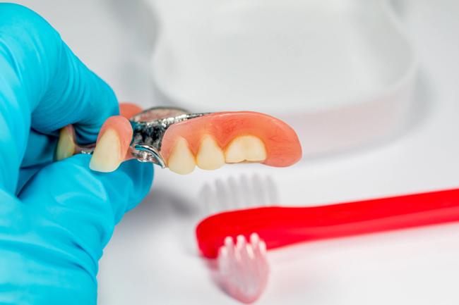 a person is holding a denture in their hand next to a red toothbrush .