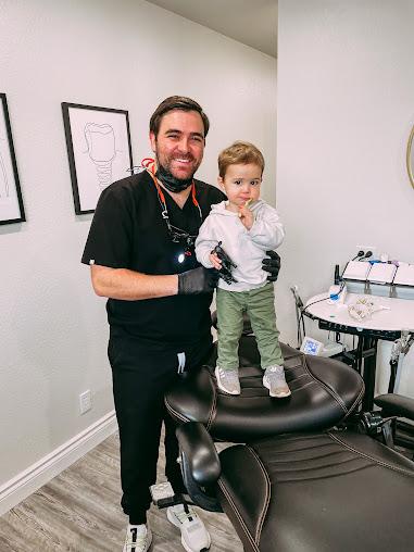 a dentist is holding a little boy in his arms in a dental office .