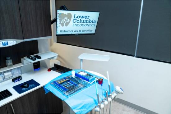 Modern dental operatory with a monitor displaying "Lower Columbia Endodontics" and a tray of instruments on a blue drape.