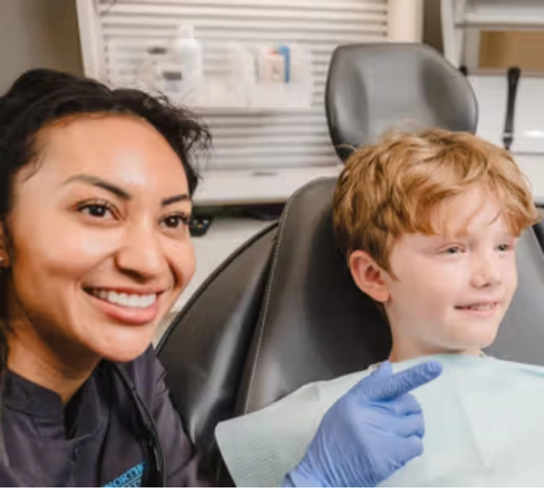 a female dentist is talking to a young boy in a dental chair .