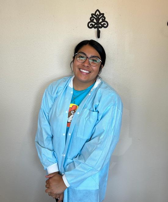 a woman wearing glasses and a blue lab coat is smiling in front of a wall .
