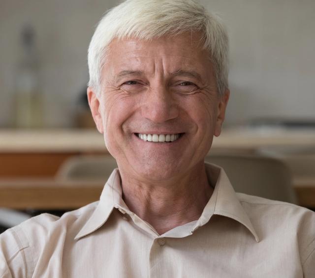 an elderly man is smiling for the camera while sitting on a couch .