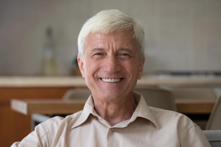 an elderly man is smiling for the camera while sitting on a couch .