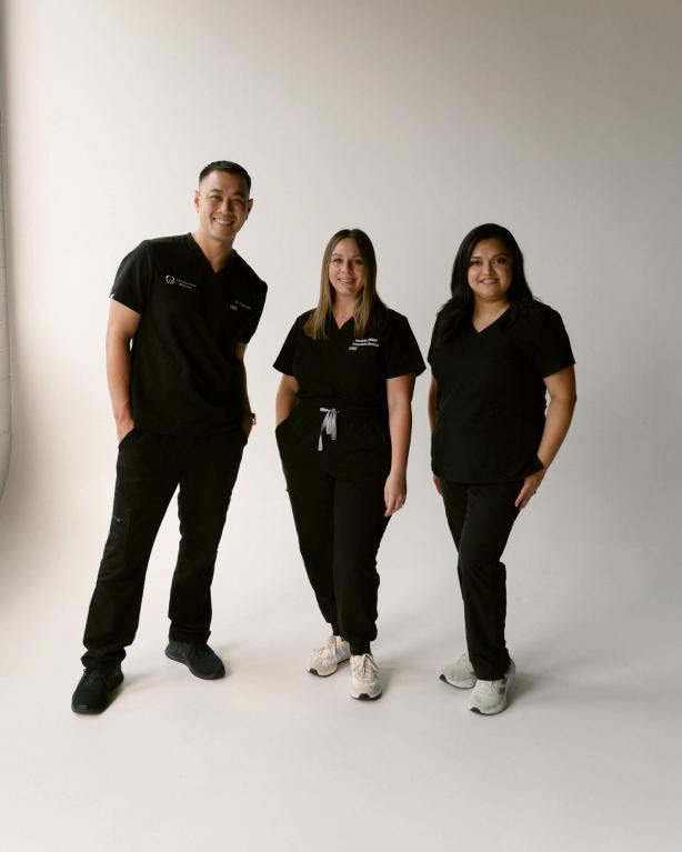 three people wearing black scrubs are posing for a picture .
