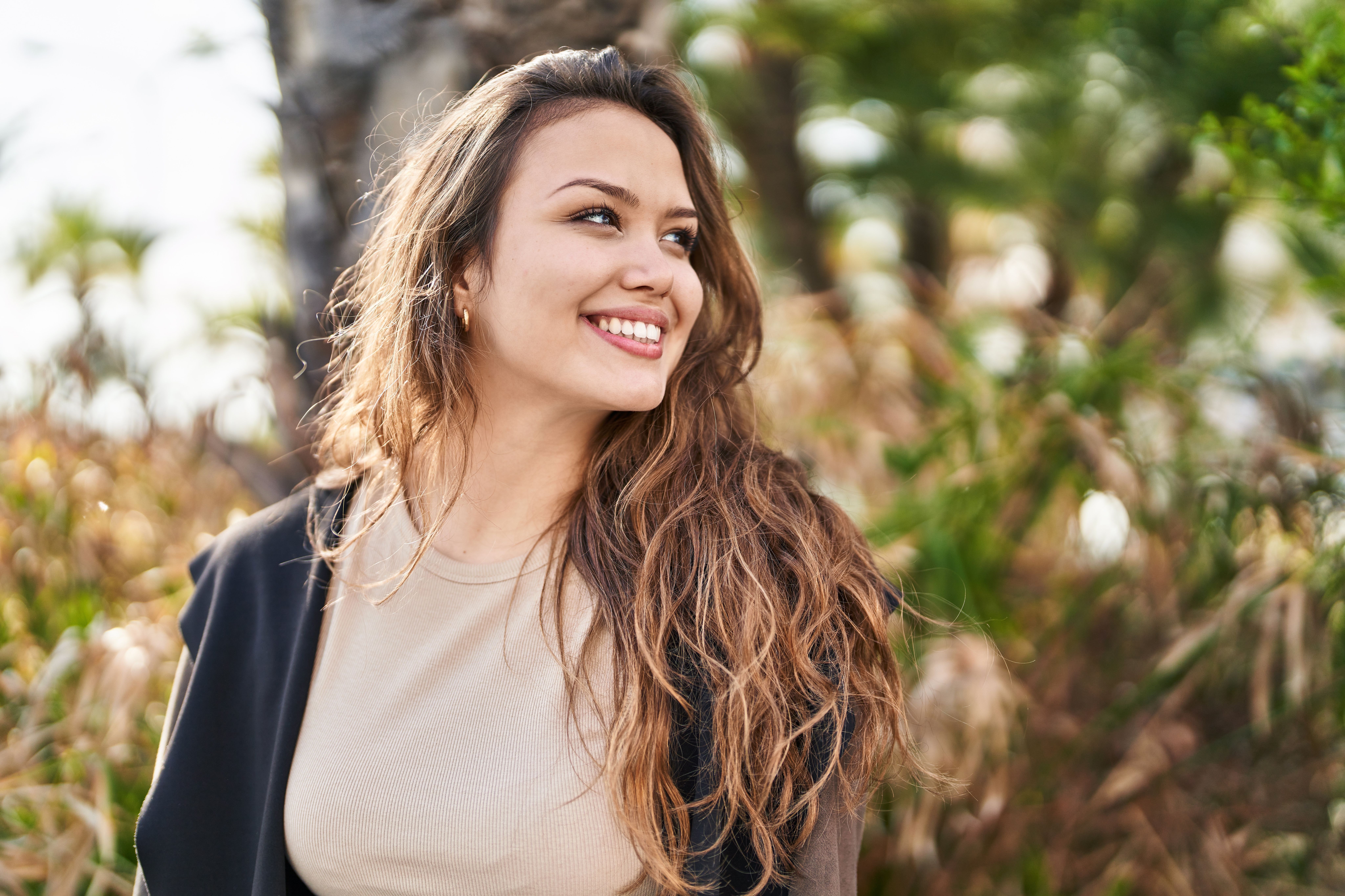 Smiling woman with long wavy hair looking right outdoors.