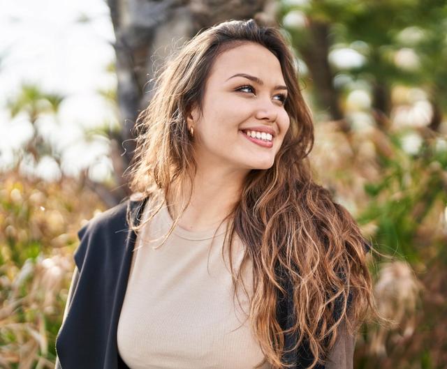 a woman with long hair is smiling while standing in a park .