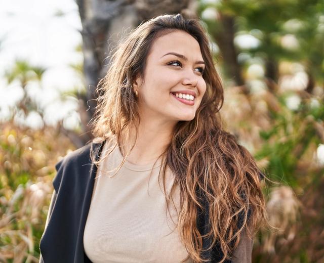a woman with long hair is smiling while standing in a park .