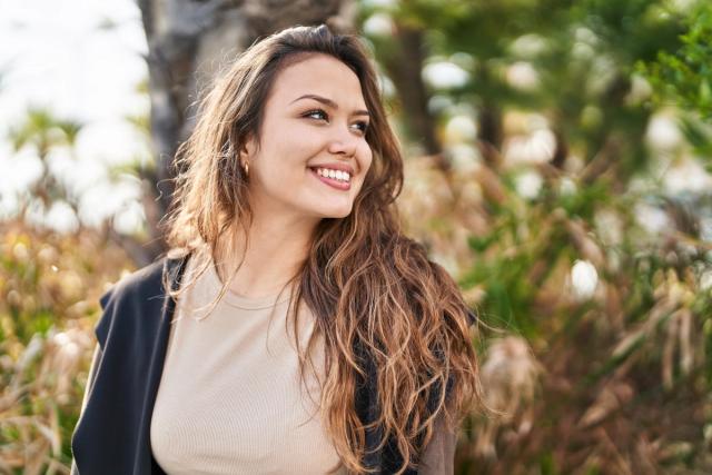 a woman with long hair is smiling while standing in a park .