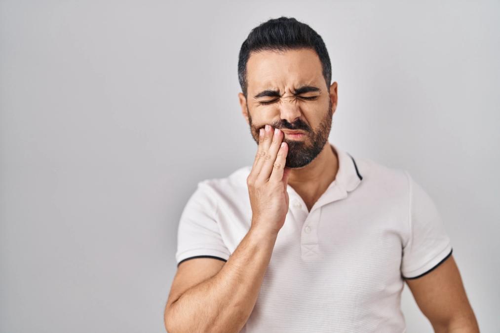 a man with a beard is holding his mouth in pain because of a toothache .