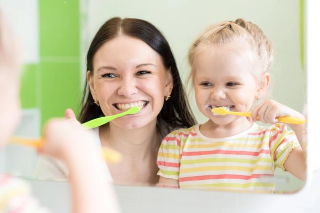 a woman and a little girl are brushing their teeth in front of a mirror .